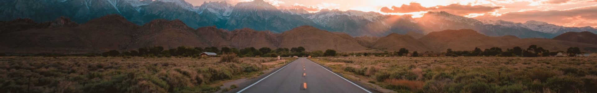 A straight road in the middle of the desert with magnificent mountains and the sunset in the background